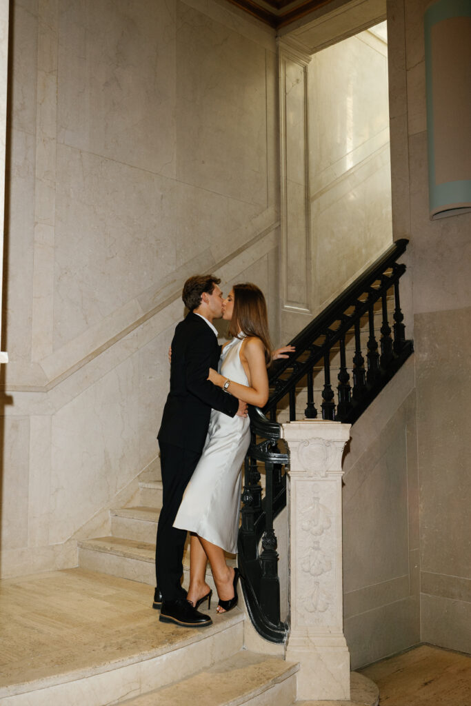 Engaged couple sharing a kiss on the marble staircase at Book Tower during their Detroit Book Tower engagement session