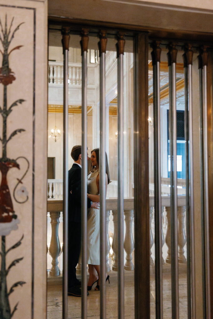 Engaged couple's reflection on ornate elevator gate mirror at Book Tower during their Detroit Book Tower engagement session
