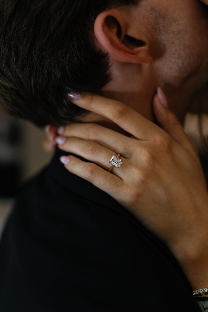 Close-up of engagement ring on bride-to-be’s hand resting on fiancé’s neck during their Detroit Book Tower engagement session