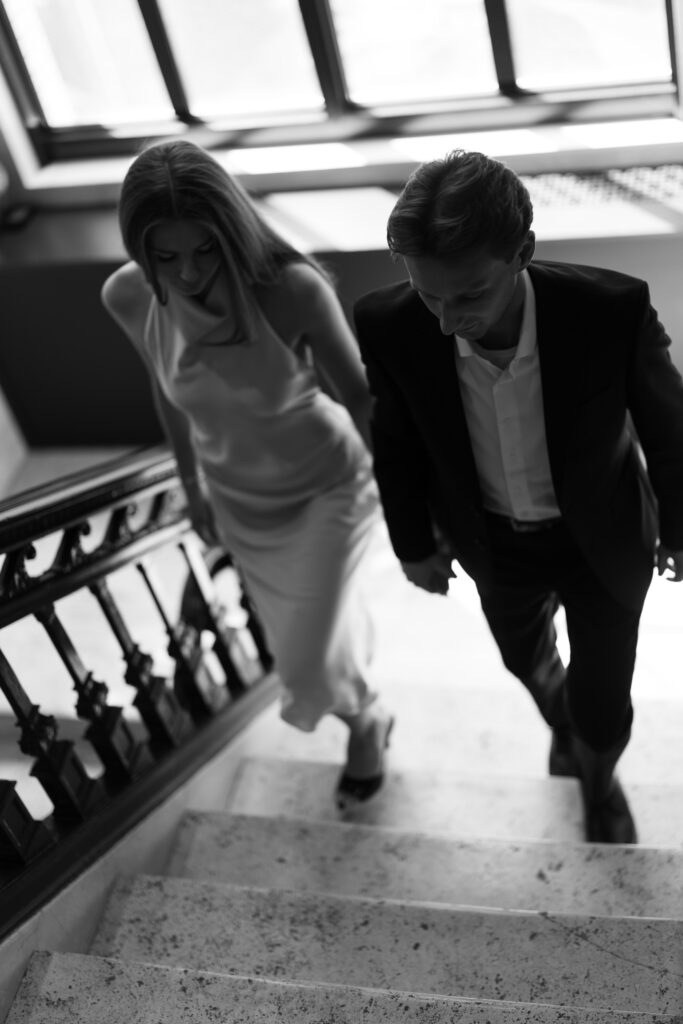 Black and white photo of engaged couple walking up marble stairs at Book Tower during their Detroit Book Tower engagement session