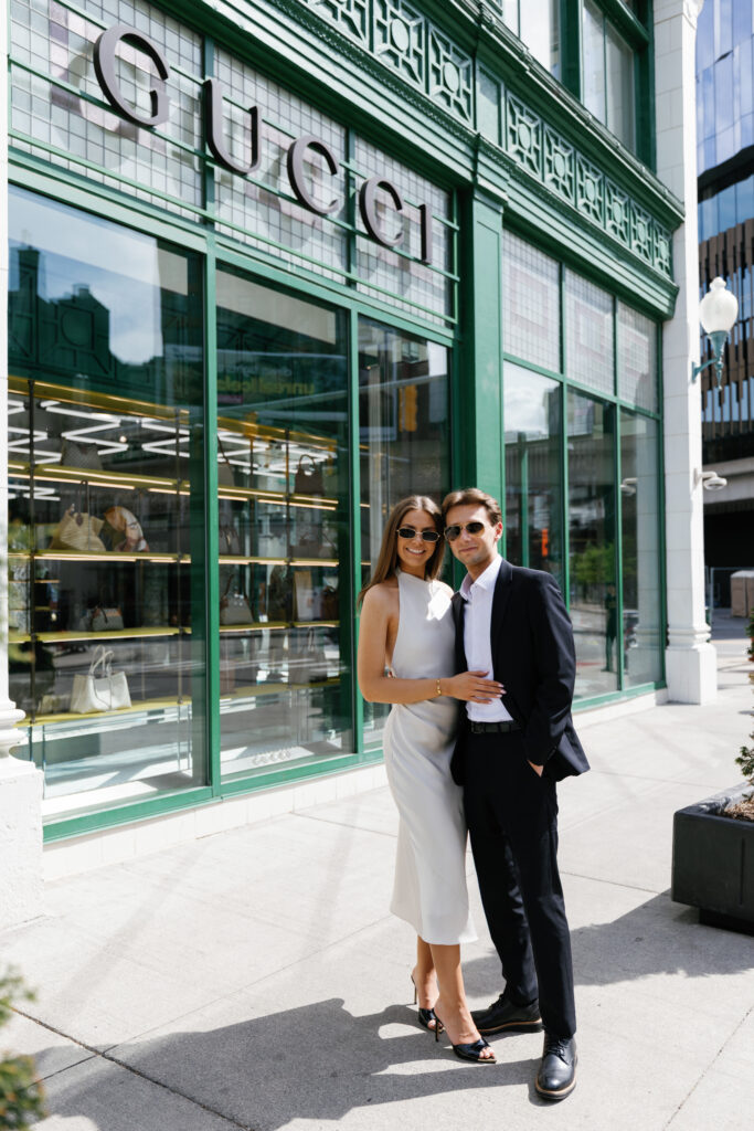 Engaged couple posing in front of the iconic green Gucci store in downtown Detroit during their Detroit Book Tower engagement session