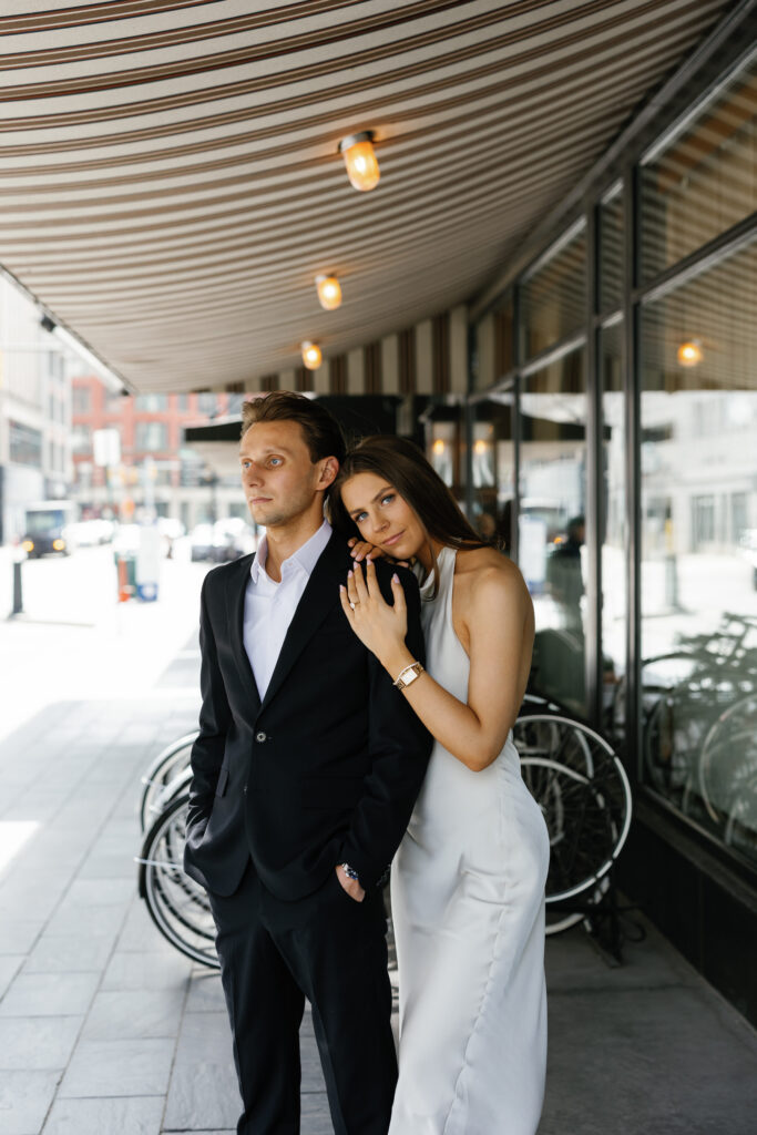 Bride-to-be leaning on her fiancé under the striped awning at Shinola Hotel in downtown Detroit during their Detroit Book Tower engagement session