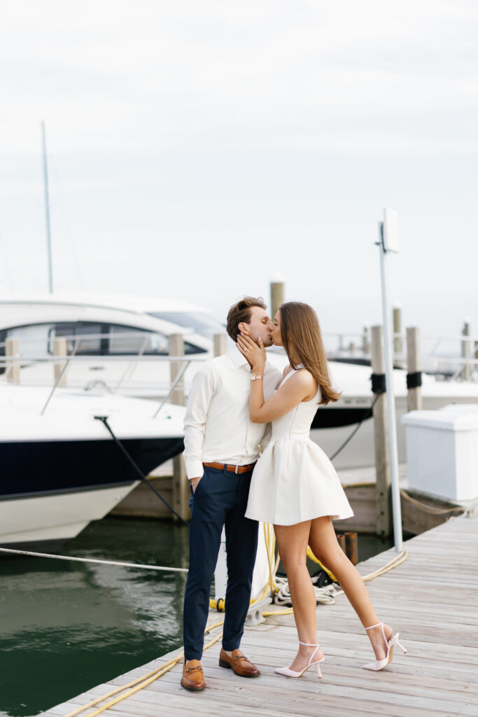 Engaged couple kissing on the dock in front of yachts at Grosse Pointe Yacht Club during their Detroit Book Tower engagement session