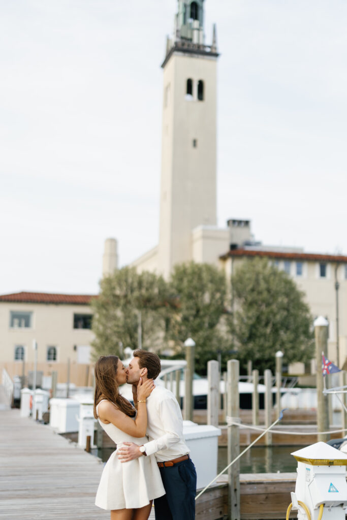 Engaged couple kissing on the dock at Grosse Pointe Yacht Club with the iconic tower in the background during their Detroit Book Tower engagement session