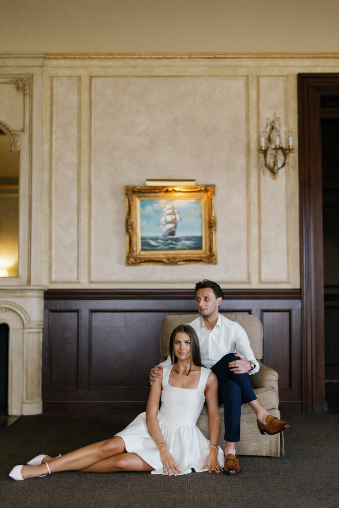 Engaged couple posing indoors at Grosse Pointe Yacht Club, seated in front of nautical artwork during their Detroit Book Tower engagement session