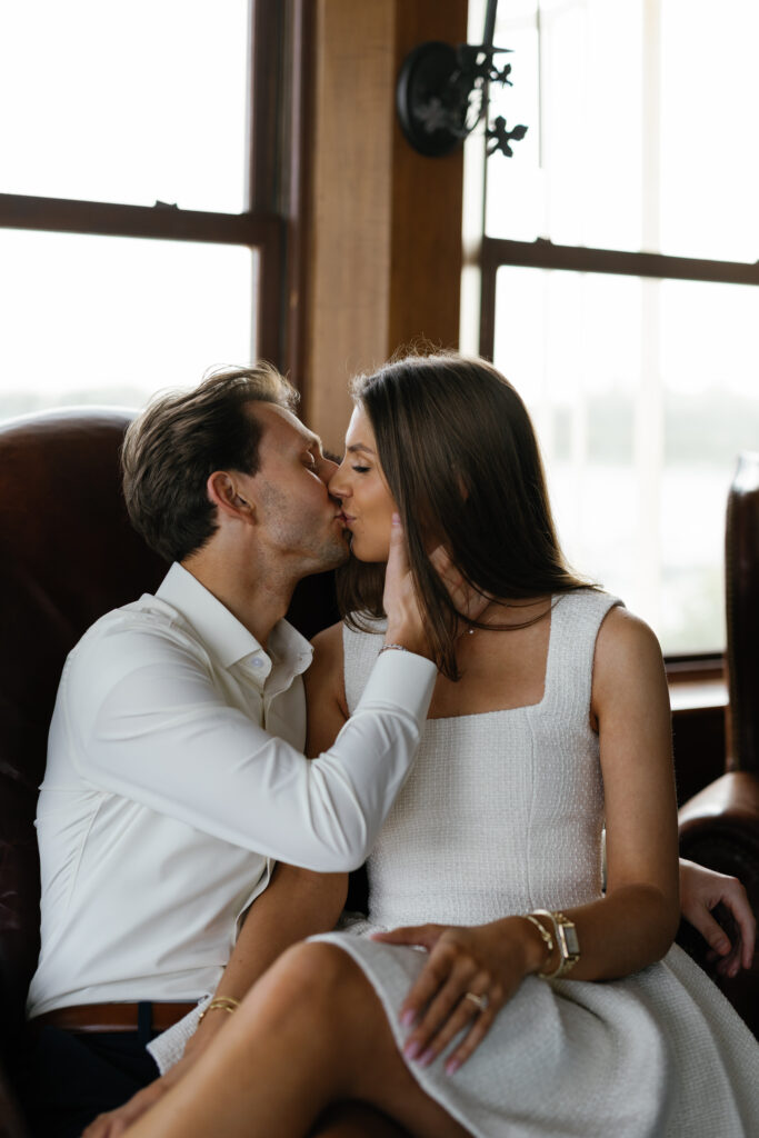 Close-up of engaged couple kissing while seated inside Grosse Pointe Yacht Club during their Detroit Book Tower engagement session