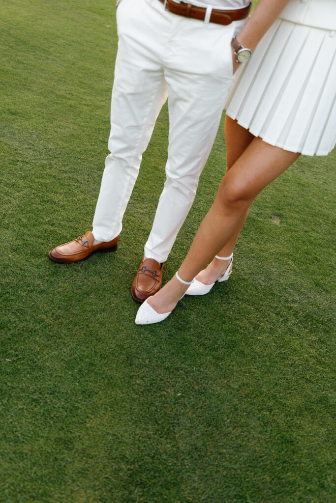 Close-up of couple’s coordinated white golf outfits and shoes on green grass at Lochmoor Golf Club during their Detroit Book Tower engagement session