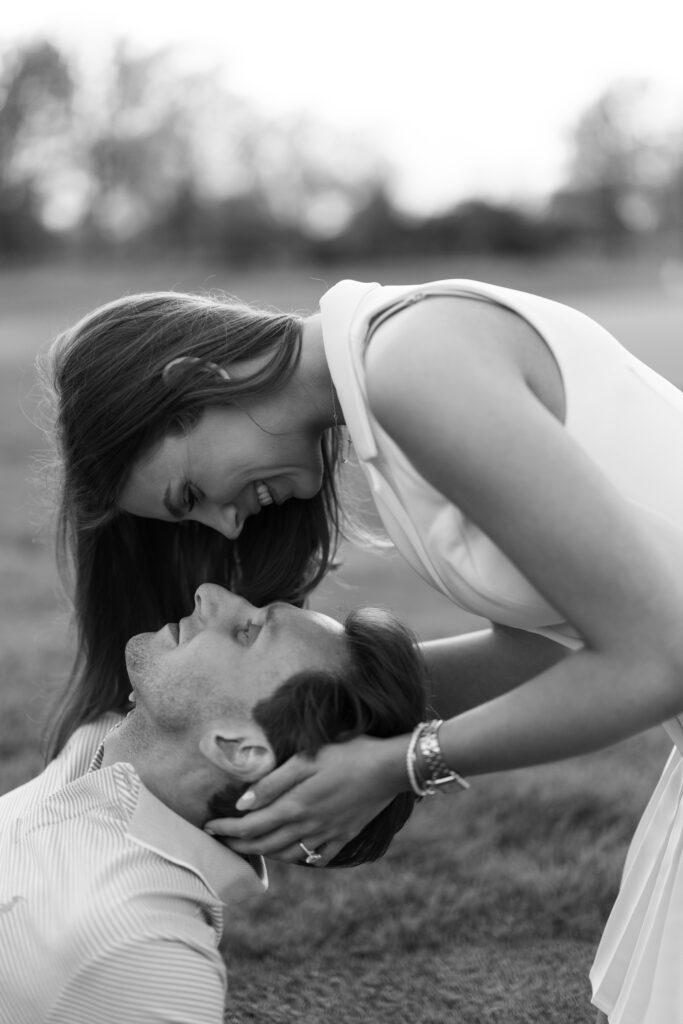 Black and white close-up of couple smiling at each other during a tender moment on the grass at Lochmoor Golf Club, part of their Detroit Book Tower engagement session