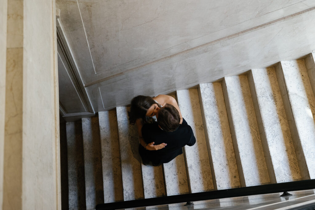 Overhead view of engaged couple embracing on marble stairs at Book Tower during their Detroit Book Tower engagement session