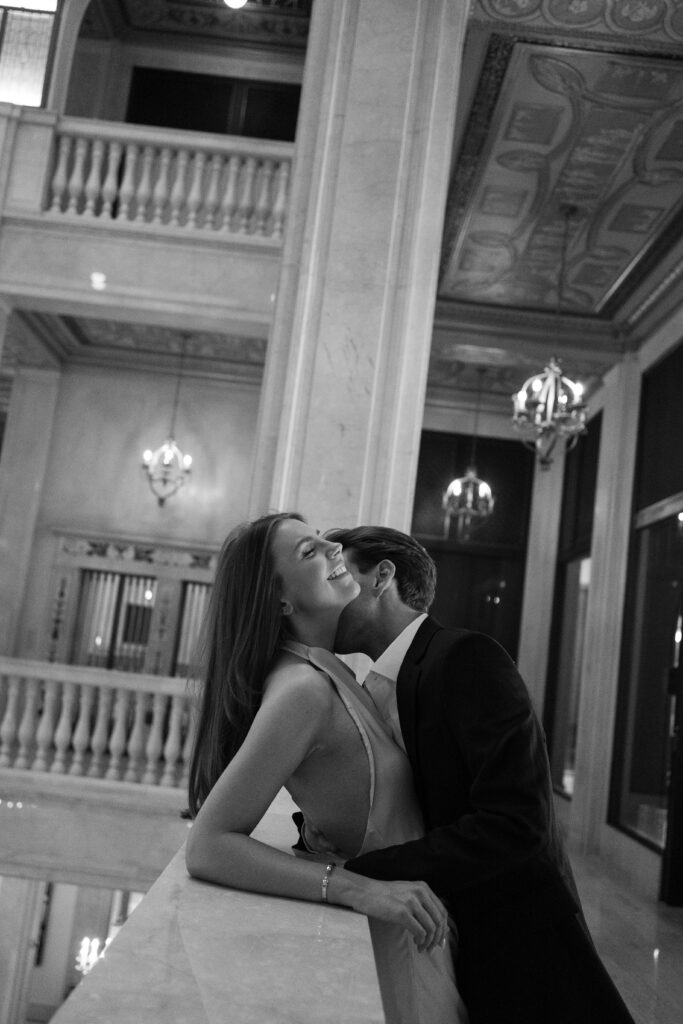 Black and white photo of engaged couple sharing a joyful moment on the marble balcony at Book Tower during their Detroit Book Tower engagement session