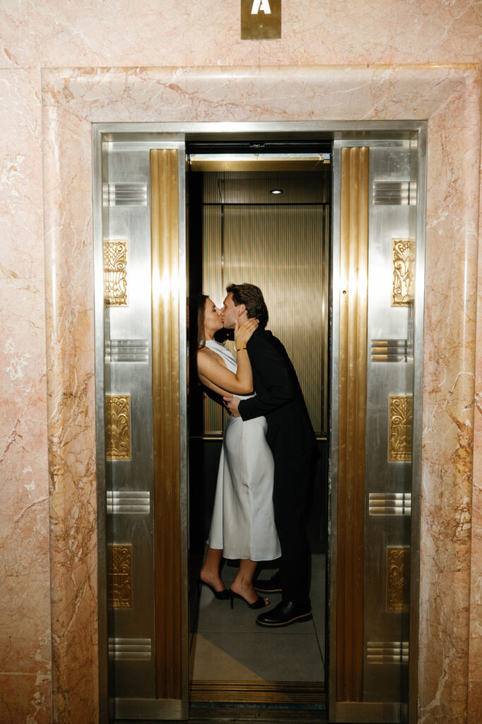 Groom-to-be kissing his fiancée inside a golden-lit elevator at Book Tower during their Detroit Book Tower engagement session