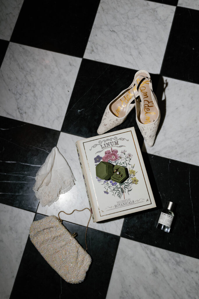 Bride's shoes, decorative book box, wedding rings, perfume, purse, hankercheif laying on checkered floor of the Graduate Hotel in Ann Arbor Michigan