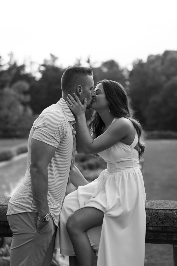 black and white Playful candid of Jeana and Micah sitting on stone ledge at Cranbrook House & Gardens.
