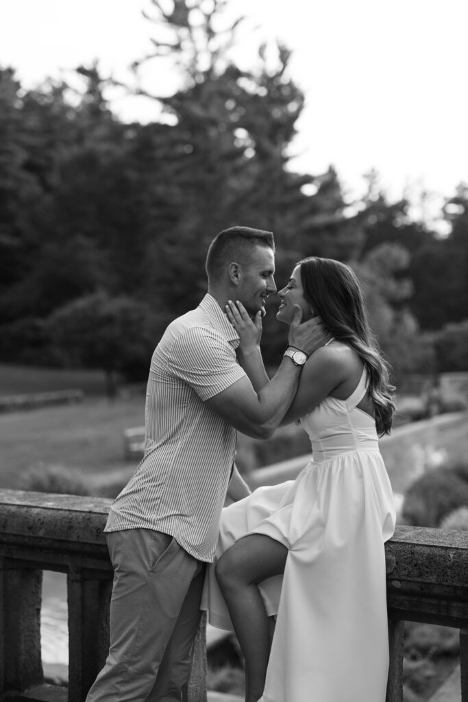 black and white bride to be sitting on stone railing sharing a kiss with groom to be