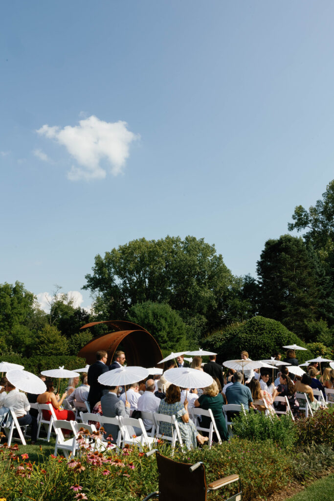 Guests seated holding parasols during wedding ceremony.