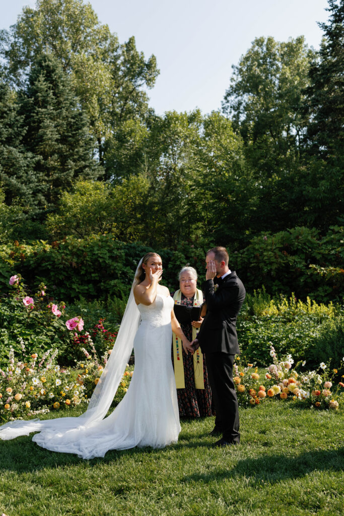 Bride blowing kiss to guests during wedding ceremony at Matthaei Botanical Garden