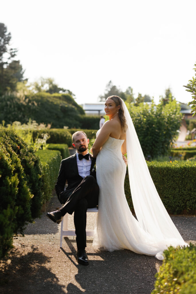 Formal Portrait of groom sitting, bride faced away from camera, looking back at camera. Portrait at Matthaei Botanical Gardens.