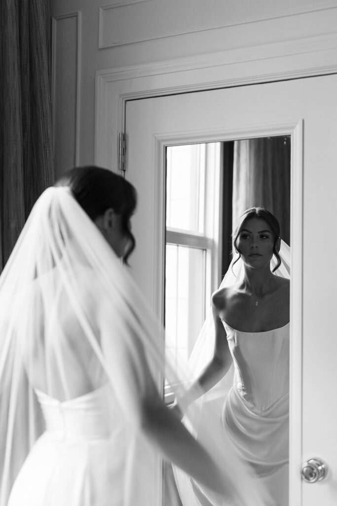 Bride in strapless gown and veil gazing at her reflection in the mirror before ceremony at Amway Grand Plaza wedding
