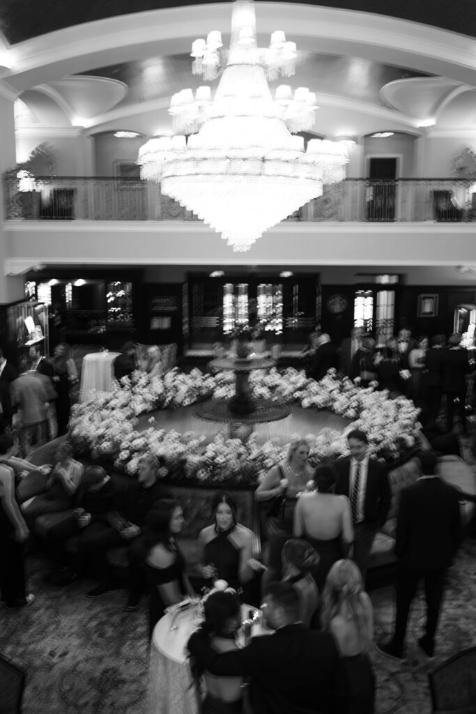 Overhead view of cocktail hour in the Patlind Lobby featuring fountain floral installation and grand chandelier at the Amway Grand Plaza