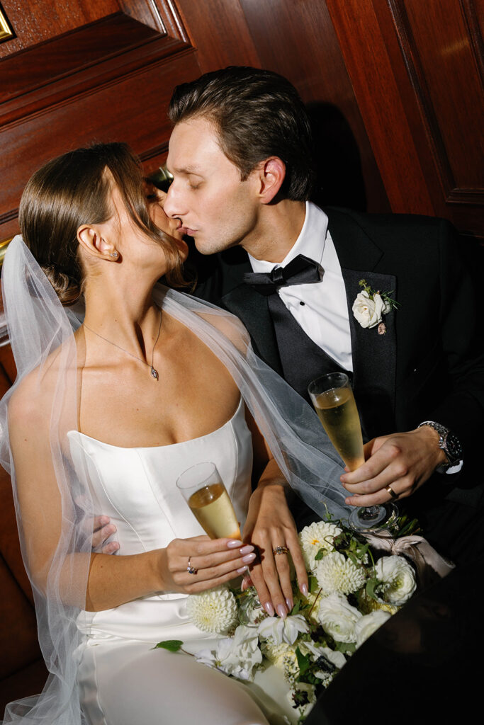 Bride and groom sharing a kiss while holding champagne glasses during cocktail hour at the Amway Grand Plaza wedding