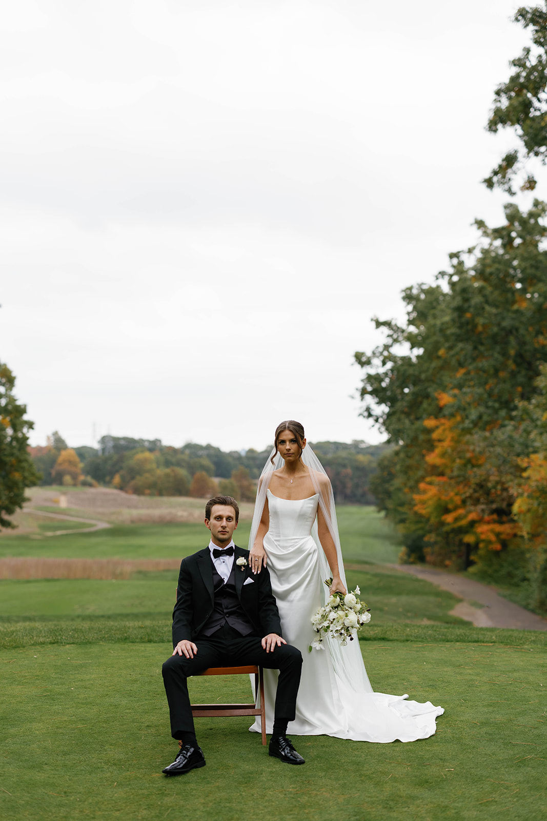 Editorial-style portrait of bride standing beside seated groom at The Mines Golf Course during Amway Grand Plaza wedding