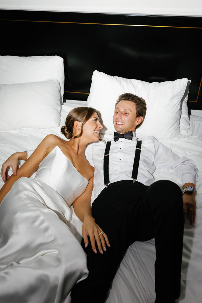 Bride and groom relaxing together on hotel bed after their Amway Grand Plaza wedding reception, smiling in post-celebration bliss