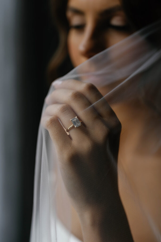 Close-up of bride’s hand holding veil, showcasing emerald-cut engagement ring before Amway Grand Plaza wedding ceremony