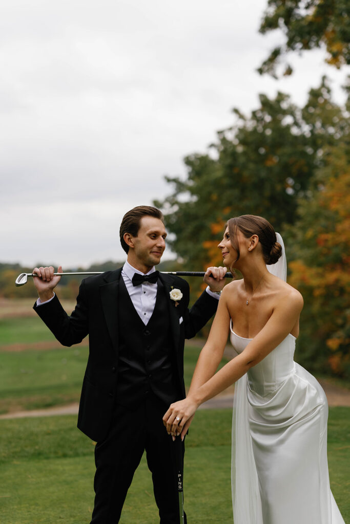 Close-up of bride and groom smiling while holding golf clubs at The Mines Golf Course during Amway Grand Plaza wedding