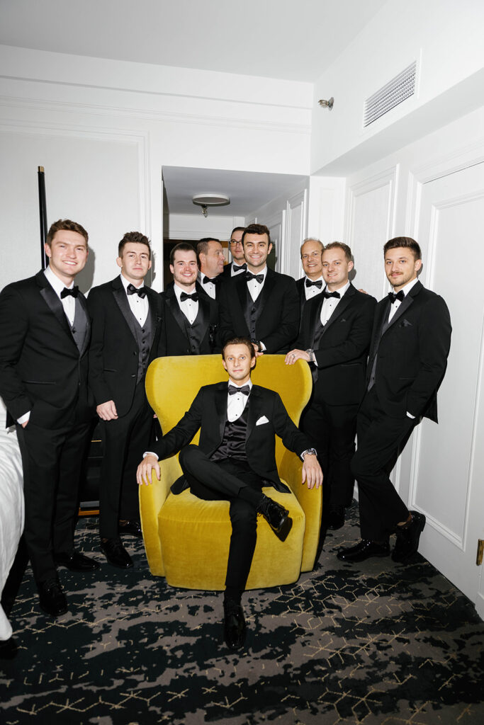 Groom seated in a hotel room at the Amway Grand Plaza with groomsmen standing around him for editorial flash portraits