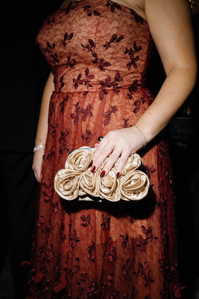 Guest in red embroidered gown holding gold floral clutch during Amway Grand Plaza wedding reception