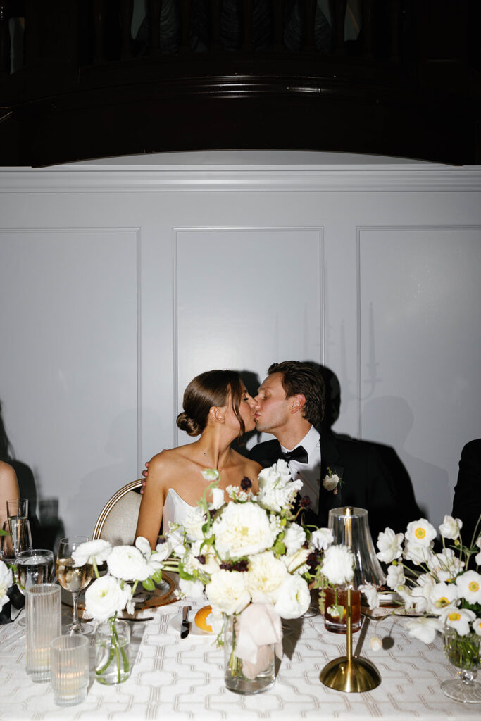 Bride and groom sharing a kiss at their head table adorned with white florals and candlelight at Amway Grand Plaza wedding