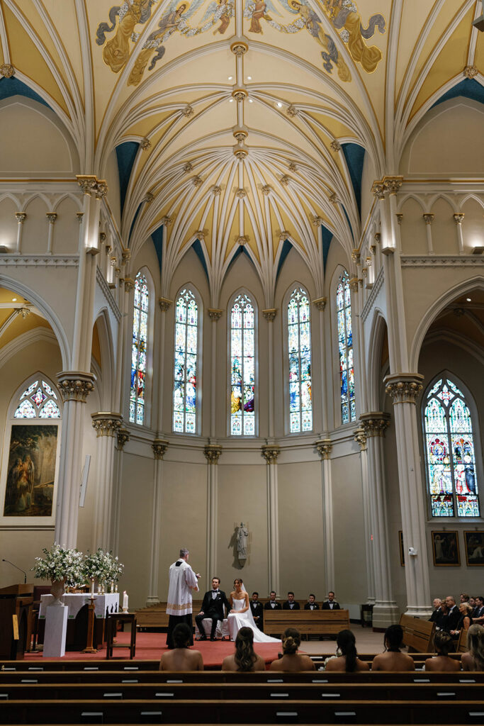 Bride and groom seated at the altar during ceremony at St. Alphonsus Church in Grand Rapids for their Amway Grand Plaza wedding