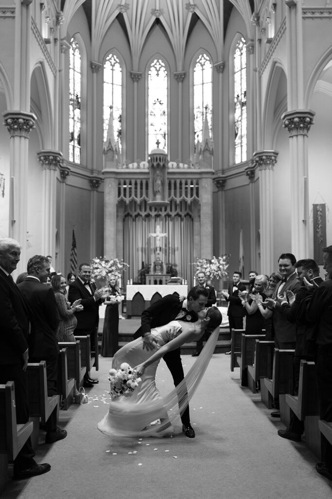 Bride and groom share a dramatic dip kiss during their ceremony exit at St. Alphonsus Church in Grand Rapids before their Amway Grand Plaza wedding reception