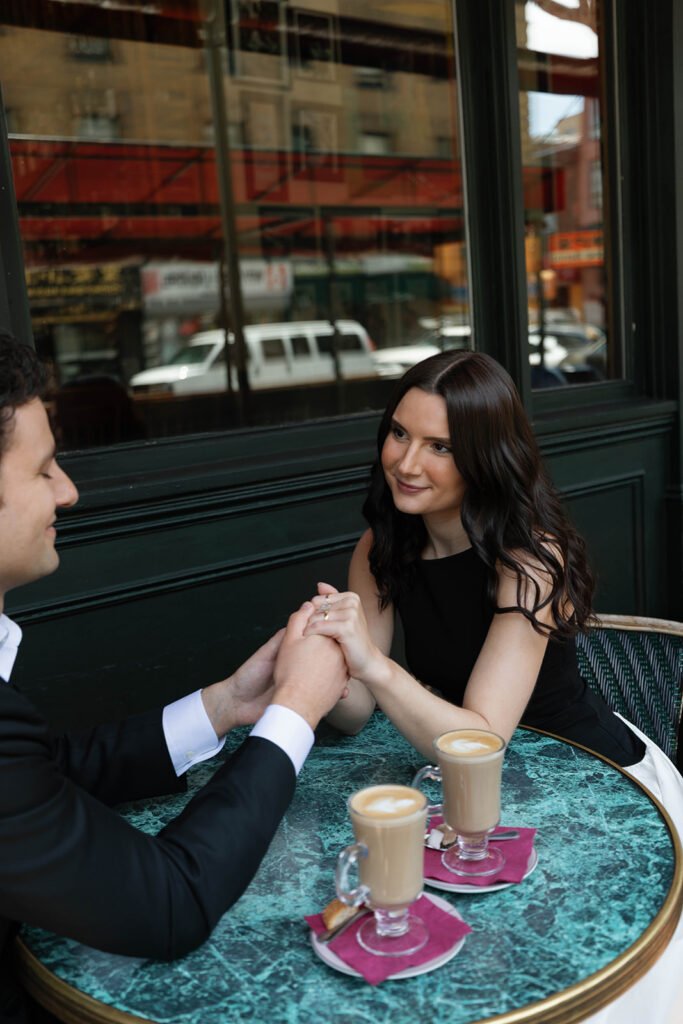 Engaged couple holding hands across a green marble cafe table at Cafe Zoetrope in San Francisco, two lattes between them in the North Beach neighborhood