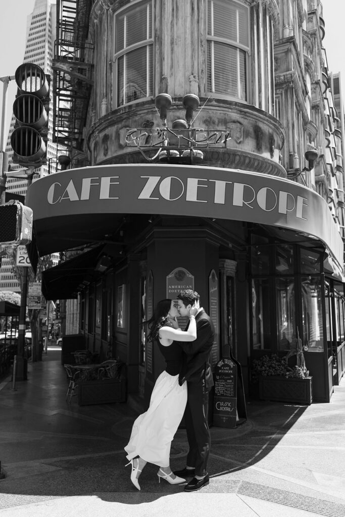 Black and white photo of an engaged couple sharing a dramatic dip kiss in front of Cafe Zoetrope in San Francisco's North Beach neighborhood