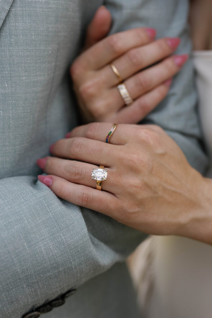 Close up detail of an engagement ring during a Filoli Gardens engagement session, gold solitaire diamond ring with pink manicure resting against a light grey suit jacket