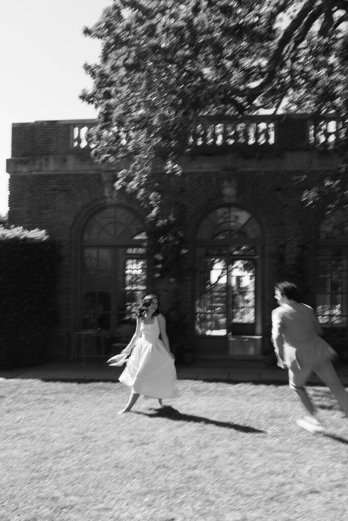 Black and white motion blur photo of an engaged couple running and laughing on the lawn in front of Filoli estate manor house in Woodside California